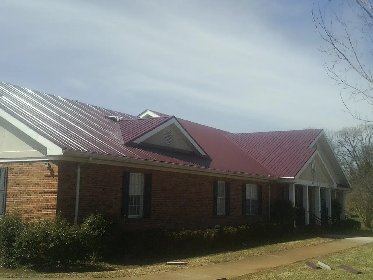 Red metal roof with gabled entries on a long brick building, from a Hail Damage Roof Repair job in Mission