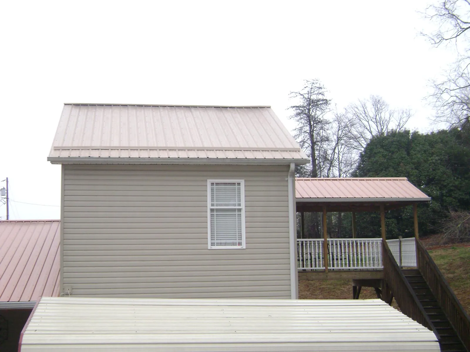 Tan metal roofs on a two story addition and attached porch, from a Roof Replacement job in Mission